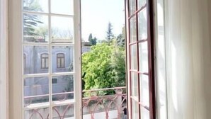 Een kamer met een groot raam en een balkon met een metalen hekwerk.