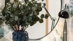 A glass table with a blue vase containing green foliage, a round mirror, and a black desk lamp. - HM - Home Feeling Studio Campanhã (Porto)