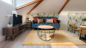 A modern loft apartment with a high ceiling, a blue sofa with red and beige cushions, a round coffee table, and a dining area with yellow chairs. - HM - Home Feeling Studio Campanhã (Porto)