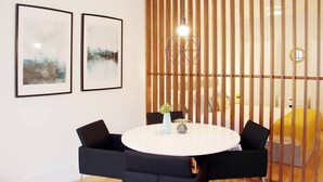 A modern room with a round table, black chairs, two framed abstract paintings, a hanging light fixture, and a wooden partition. - HM - Carlos Alberto Apartment 2 (Porto)