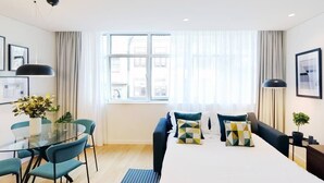 A modern hotel room with a bed, a dining table with chairs, a large window with curtains, and a small side table with a lamp. - HM - Sta Catarina Charming Apartment (Porto)