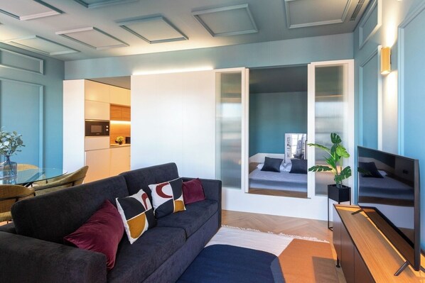 A modern living room with a sofa, a dining table, and a kitchen area.