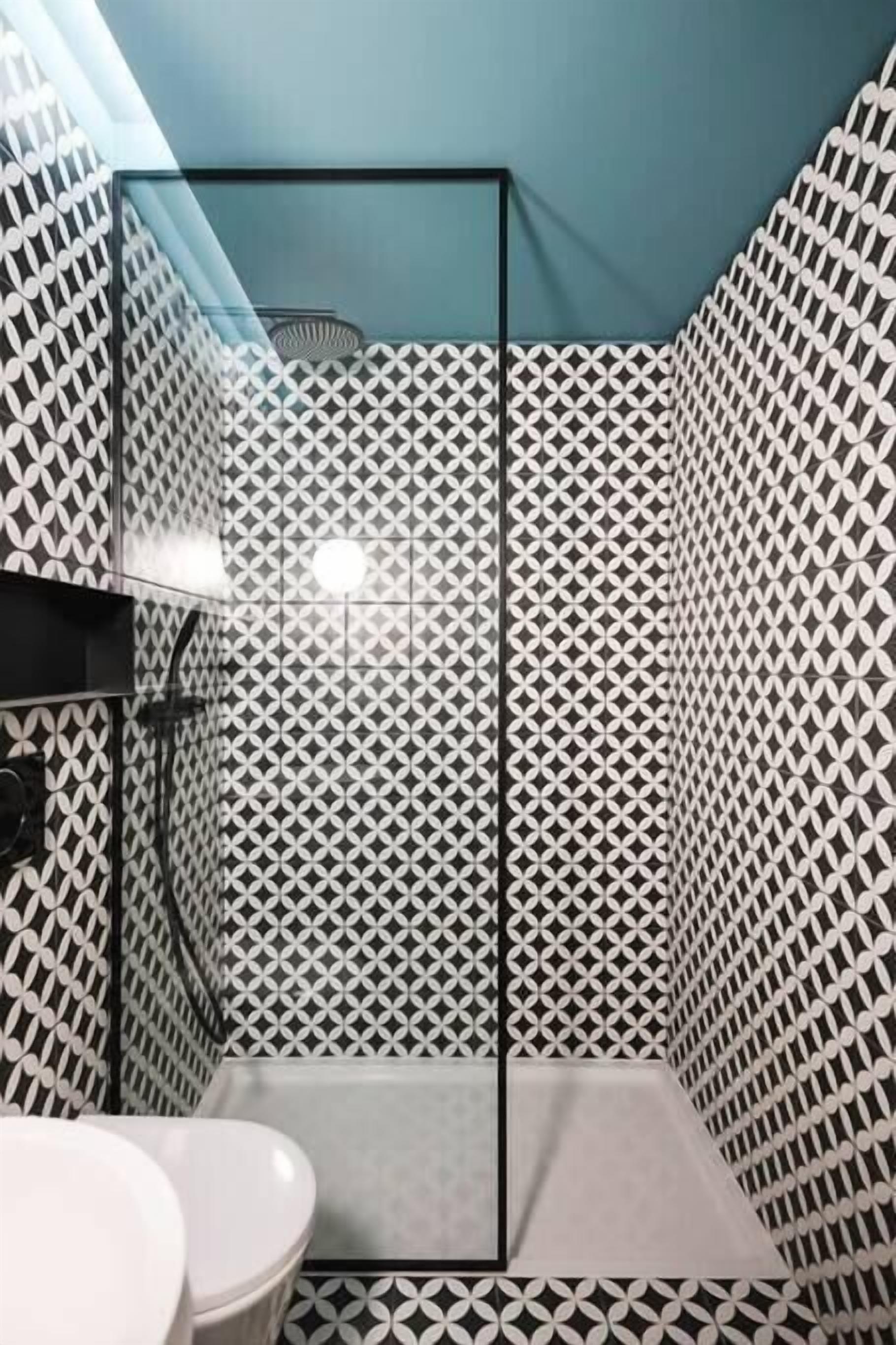 Un bagno con parete a motivo geometrico, box doccia in vetro e water bianco.