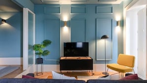 Ein Wohnzimmer mit Flachbildfernseher, Stehlampe und gelbem Sessel.