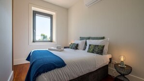 A bedroom with a bed, a window, a bedside table with a lamp, and an air conditioning unit on the wall. - HM Oporto Studio Pool Oasis (Porto)