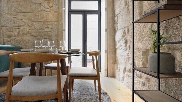 A dining area with a stone wall, a round table with chairs, and a black metal shelf with a vase. - HM - Pinheiro Downtown Living (Porto)