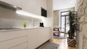 A modern kitchen with white cabinets, a black countertop, and a built-in stove. There is a dining area with a table and chairs, and a large window providing natural light. - HM - Pinheiro Downtown Living (Porto)