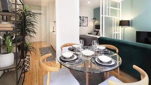 A dining area with a glass table set for four, surrounded by wooden chairs. A staircase with a metal railing is visible to the left, and a green sofa is in the background. - HM - Pinheiro Downtown Living (Porto)