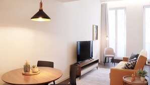 Una sala de estar moderna con una mesa redonda de madera, un sofá, un televisor y una lámpara colgante.