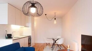 A modern living room with a blue sofa, wooden flooring, a dining area with white chairs, and a kitchen in the background. - HM – Historic Downtown Batalha Studio (Porto)