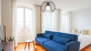 A modern living room with a blue sofa, a small round table, and a bed with patterned pillows. - HM – Historic Downtown Batalha Studio (Porto)