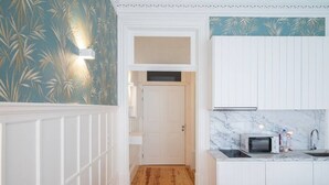 A narrow hallway with a wooden floor leading to a white door. A small seating area with a blue cushion is visible. - HM Loios charming loft (Porto)