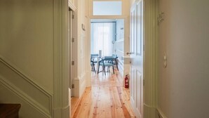 A hallway with wooden flooring, white walls, and a door leading to a dining area with blue chairs and a table. - HM Loios charming loft (Porto)