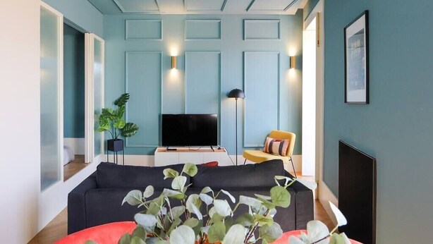 Ein modernes Wohnzimmer mit einem dunklen Sofa, einem Flachbildfernseher und einem roten Ottomanen.