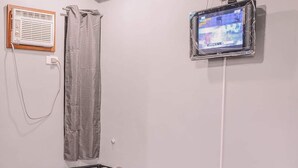 Ein Einzelbett mit einem herzförmigen Handtuch, einem an der Wand befestigten Fernseher und einer Duschvorhang.