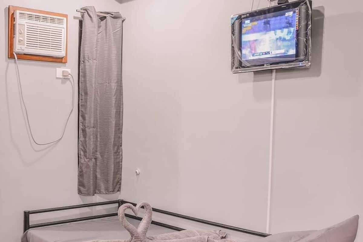 Una cama individual con una toalla con forma de corazón, un televisor fijado a la pared y una cortina de ducha.
