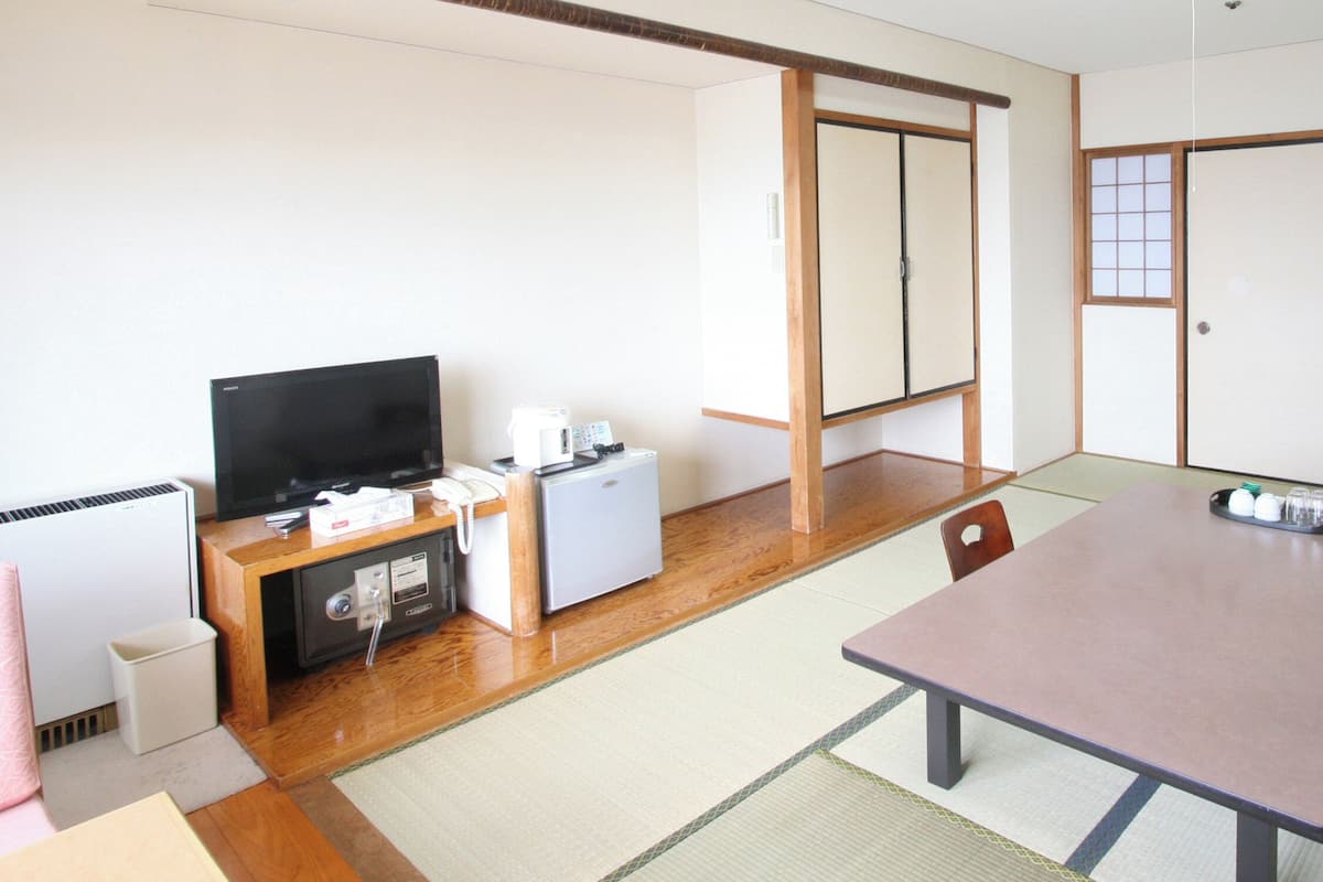A traditional Japanese-style room with tatami flooring, a low table, a television, a small refrigerator, and sliding doors.