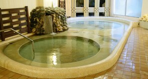 A hot tub with a stone waterfall feature, a wooden bench, and tiled flooring. - Hotel Nankaiso (Minamiboso)