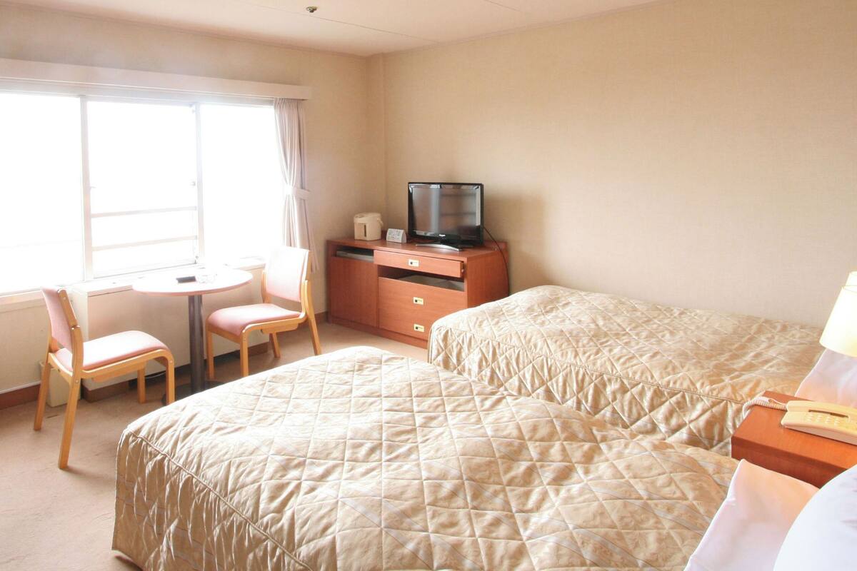 A hotel room with two beds, a desk with a chair, a television, and a lamp.