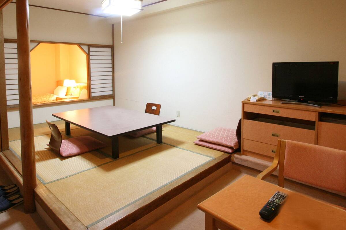 A traditional Japanese room with tatami flooring, a low table, a chair, a television, and a cabinet.