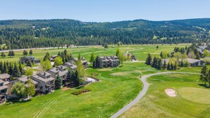 Ein Golfplatz mit Wohnhäusern, blauem Himmel und bewaldeten Hügeln im Hintergrund.
