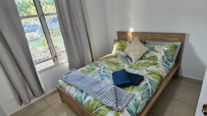 A bedroom with a bed, curtains, an air conditioning unit, and a view through a window. - Yiayi's House Getaway (Wagaman)