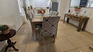 A dining area with a wooden table and patterned chairs, a kitchen in the background, and a mirror on the wall. - Yiayi's House Getaway (Wagaman)