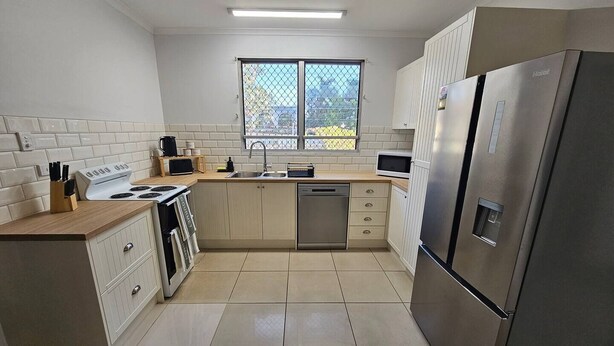 A modern kitchen with white cabinets, a stainless steel refrigerator, a dishwasher, and a stove. - Yiayi's House Getaway (Wagaman)