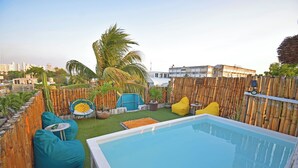 A rooftop pool area with a bamboo fence, green and yellow bean bags, and a view of the cityscape in the background. - Casa Nomis Cancun (Cancun)