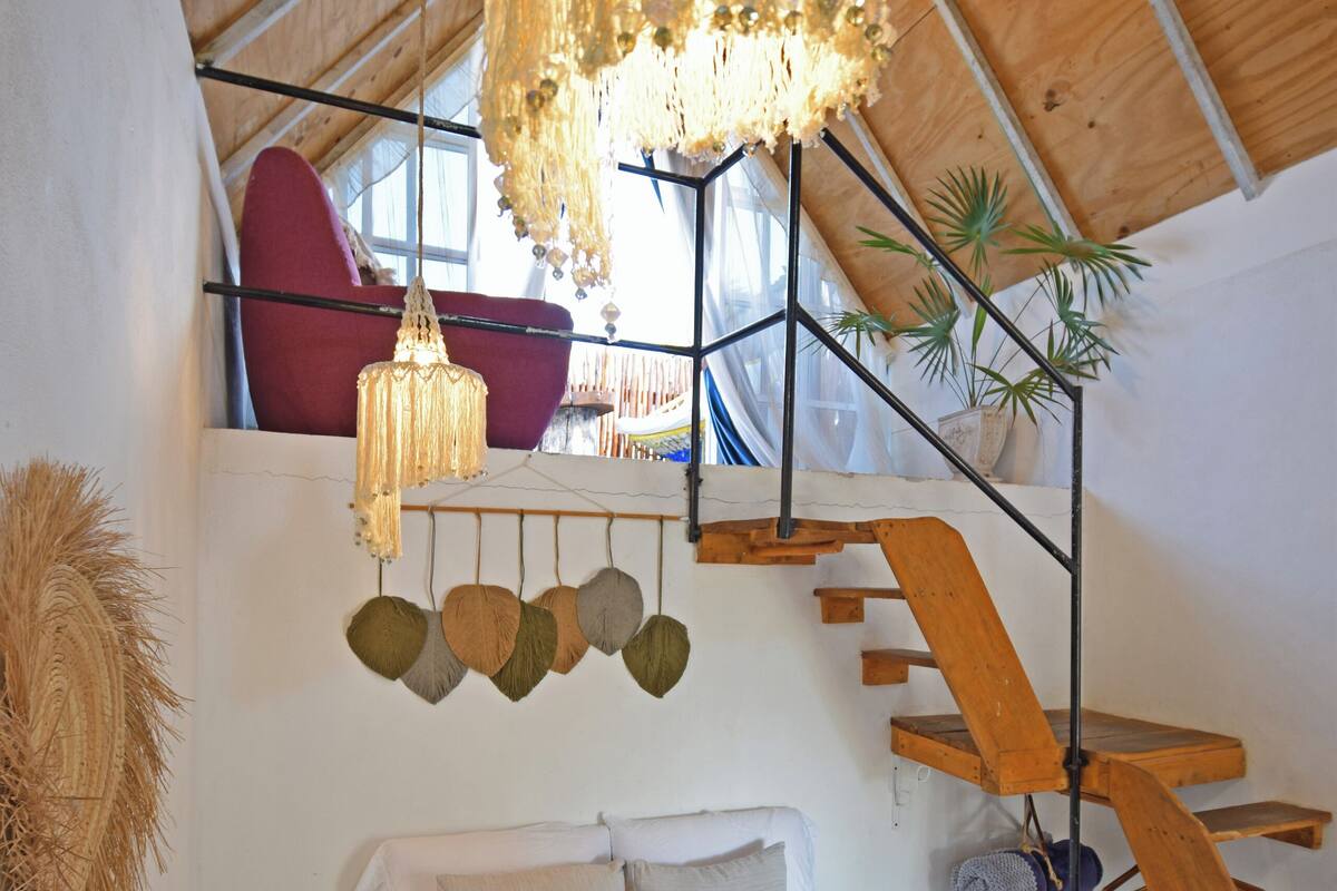 A bedroom with a bed, a hanging light fixture, a staircase, and a potted plant.
