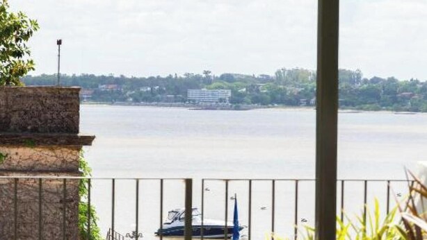 Un balcón con vistas a un río, una embarcación y un paisaje urbano distante.