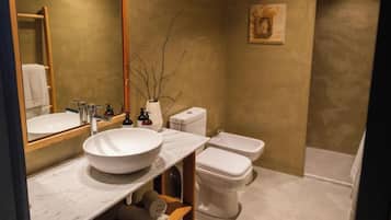A bathroom with a large white sink, two toilets, a mirror, and a small painting on the wall.