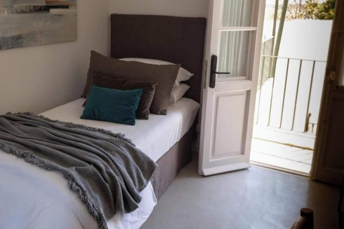 Una cama individual con una manta gris, un cabecero oscuro y varias almohadas.