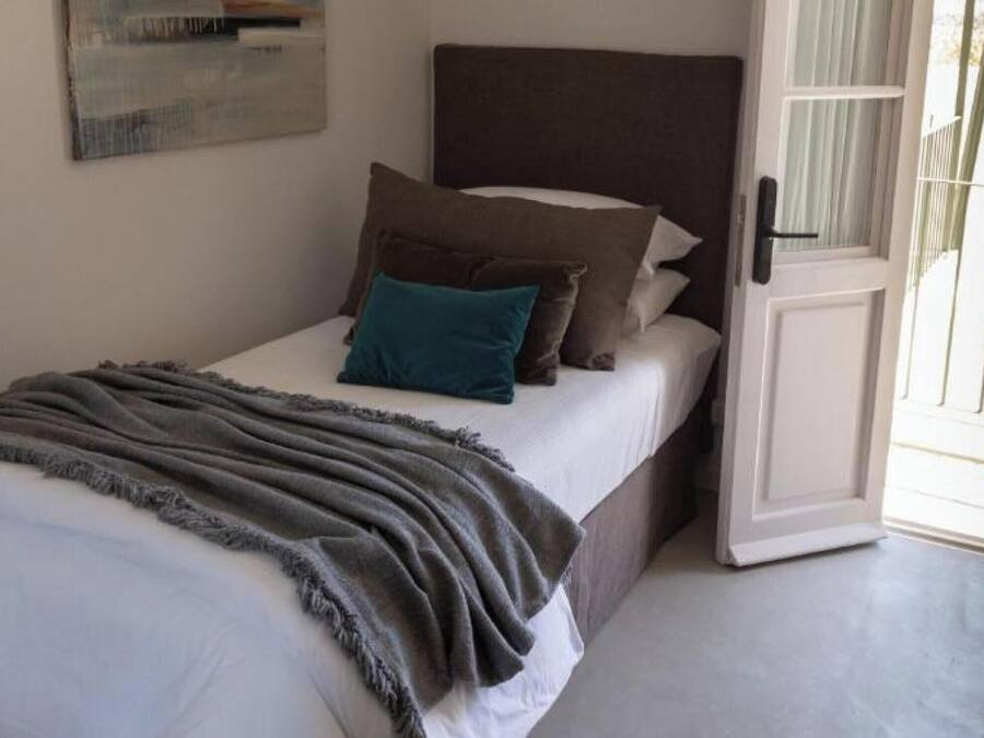 A single bed with a grey blanket, a dark headboard, and multiple pillows.