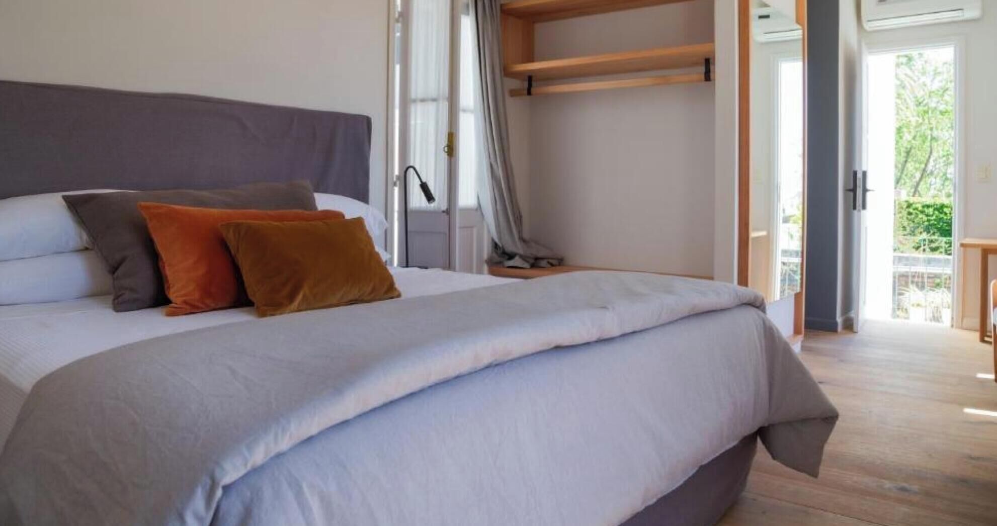 A bed with a grey headboard, multiple pillows, and a wooden shelf above it.