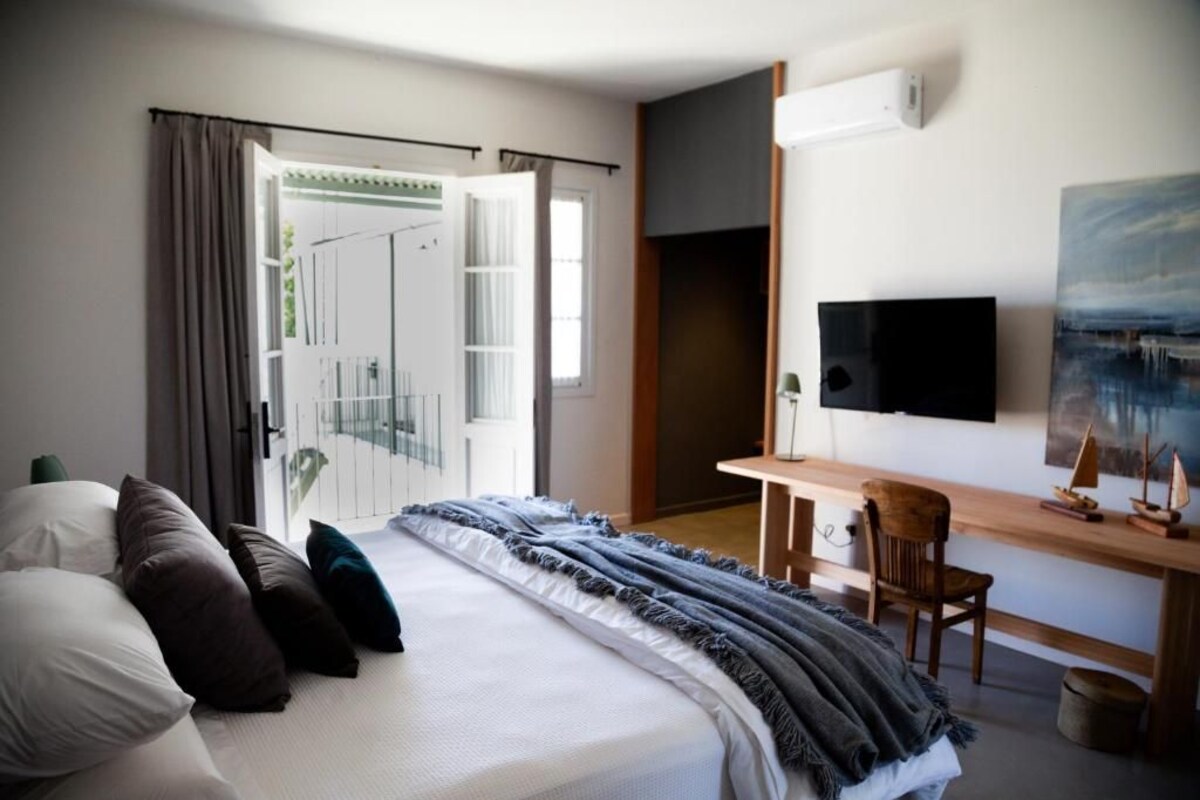 A hotel room with a bed, a desk, a chair, a TV, and a painting on the wall.