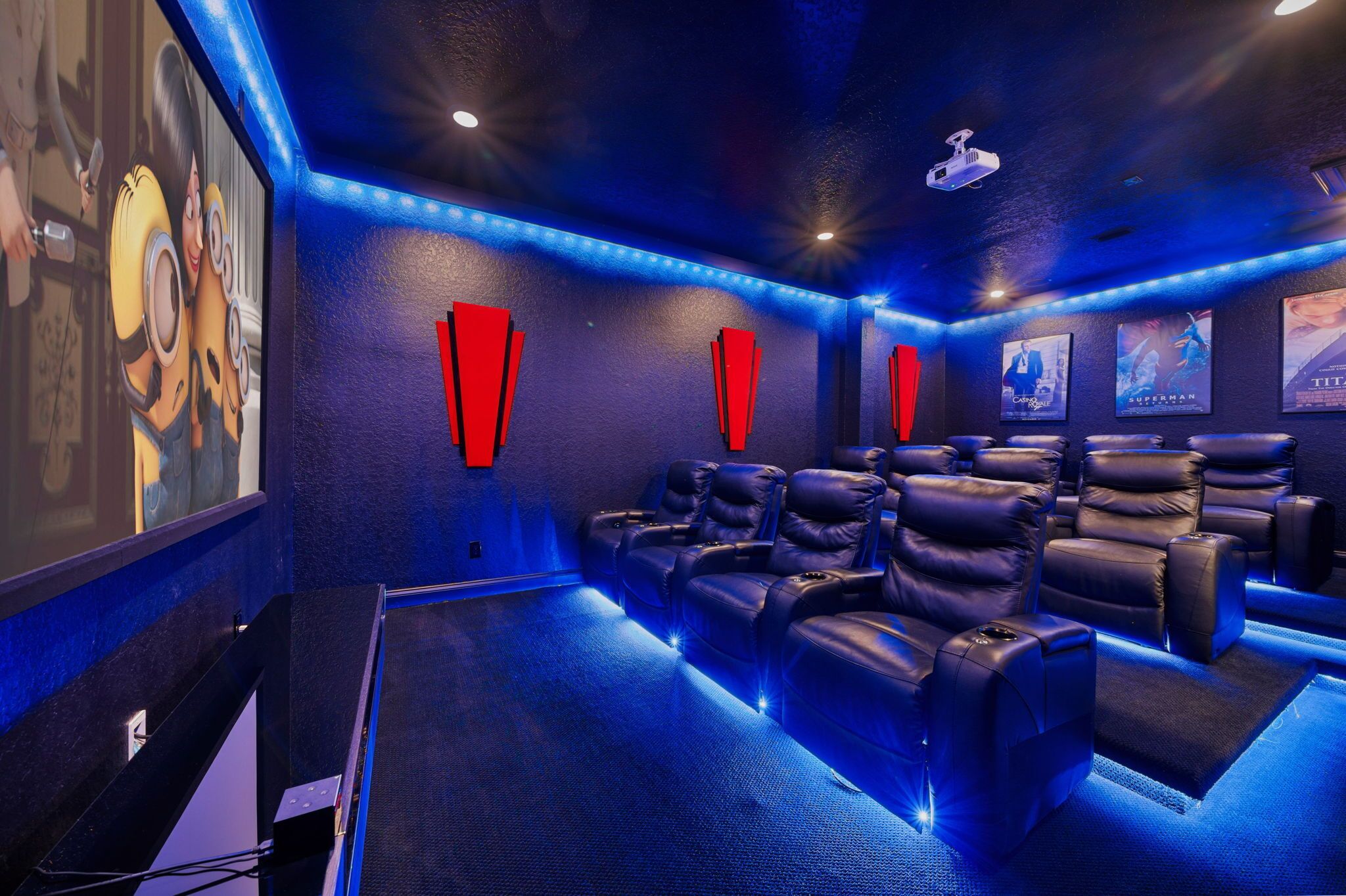 Une salle de cinéma privée dotée d’un éclairage d’ambiance bleuté, de plusieurs fauteuils en cuir inclinables et d’un grand écran.