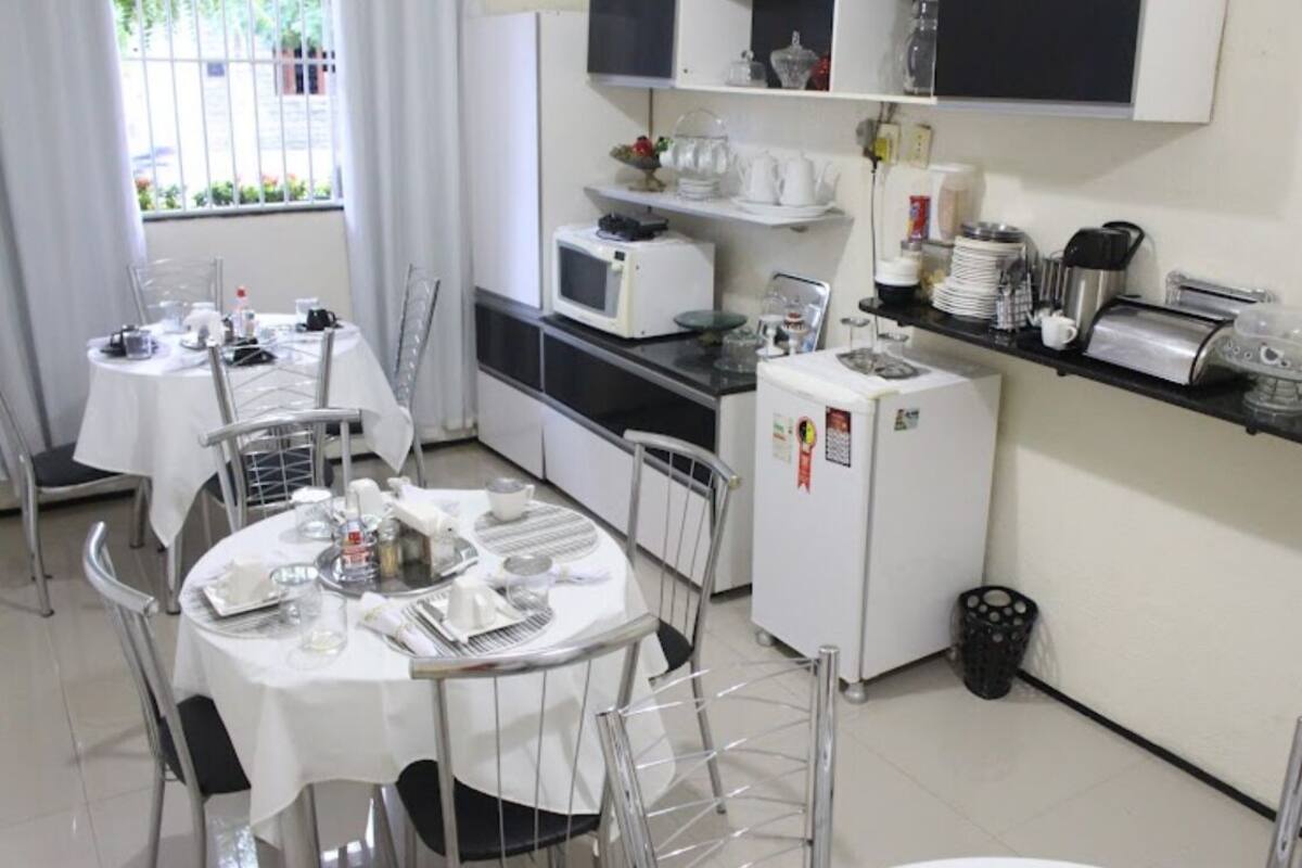 A compact kitchen with a microwave, toaster, and refrigerator. There is a dining table set with chairs.