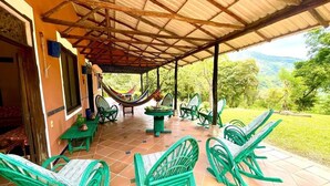 Un patio al aire libre con mobiliario de mimbre verde, una hamaca y vistas de la vegetación circundante.