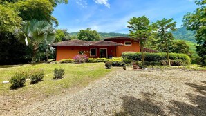 Una casa de fachada roja, rodeada por un jardín cuidado con diversas plantas y un camino de entrada de grava.