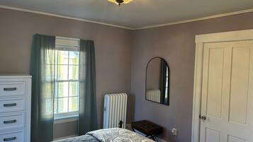 A bedroom with a bed, a dresser, a radiator, a mirror, and a door.