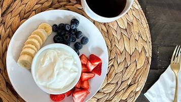 Une assiette contenant du yaourt, des tranches de bananes, des myrtilles et des fraises, une tasse de café et un set de table en fibres tressées.