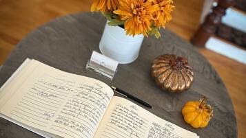Une table ronde avec un carnet, un stylo, un petit vase blanc contenant des fleurs orange et deux petites courges.
