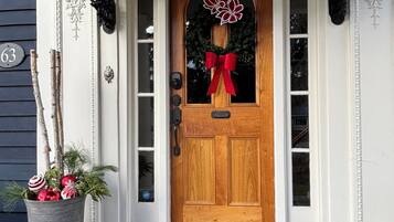 A wooden front door with a red bow, a potted plant with greenery and ornaments, and a doormat with a house design.