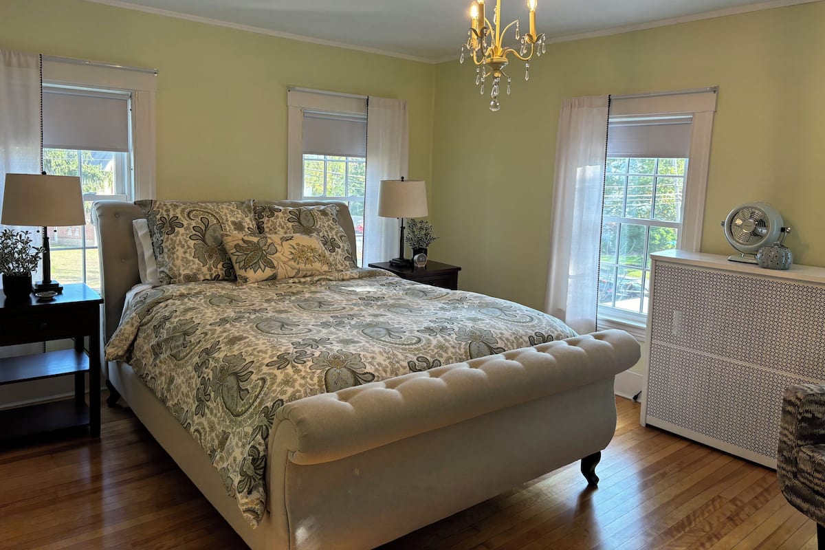 A bedroom with a large bed, two bedside tables with lamps, a chandelier, and a radiator.