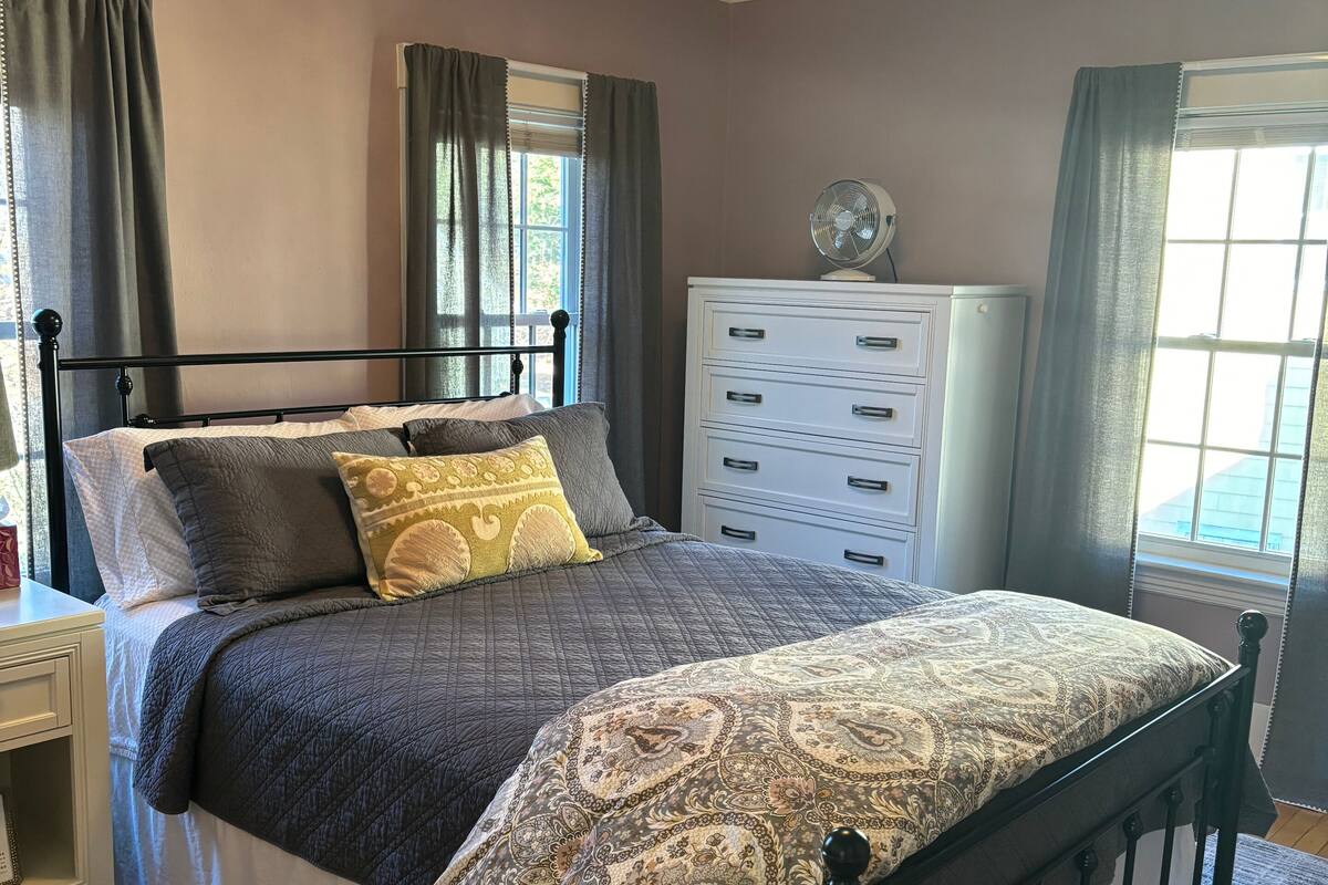 A bedroom with a bed, a dresser, a fan, and a chandelier.