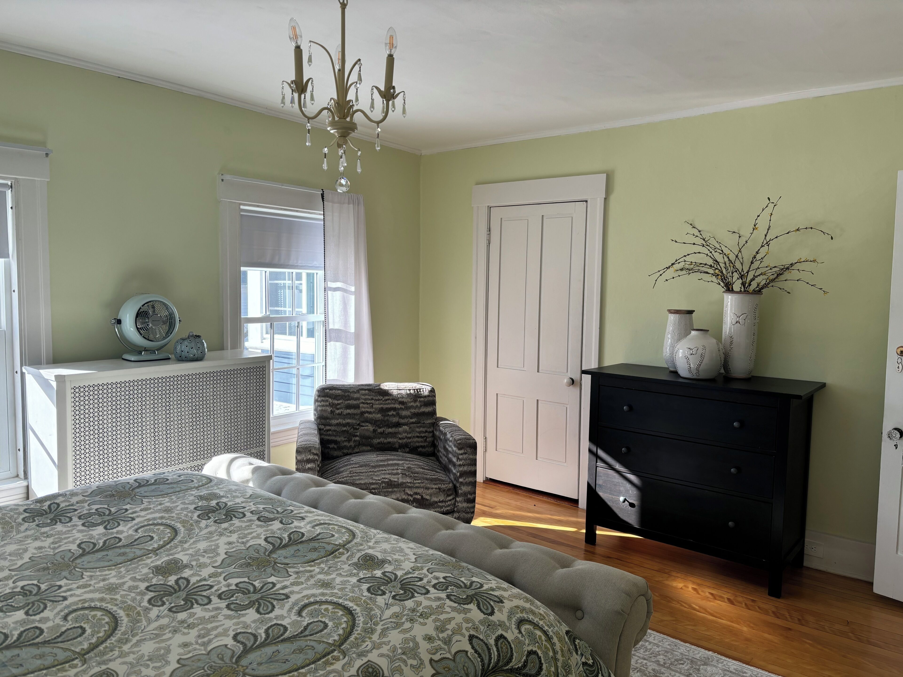 A bedroom with a bed, a chair, a dresser, and a window with curtains.