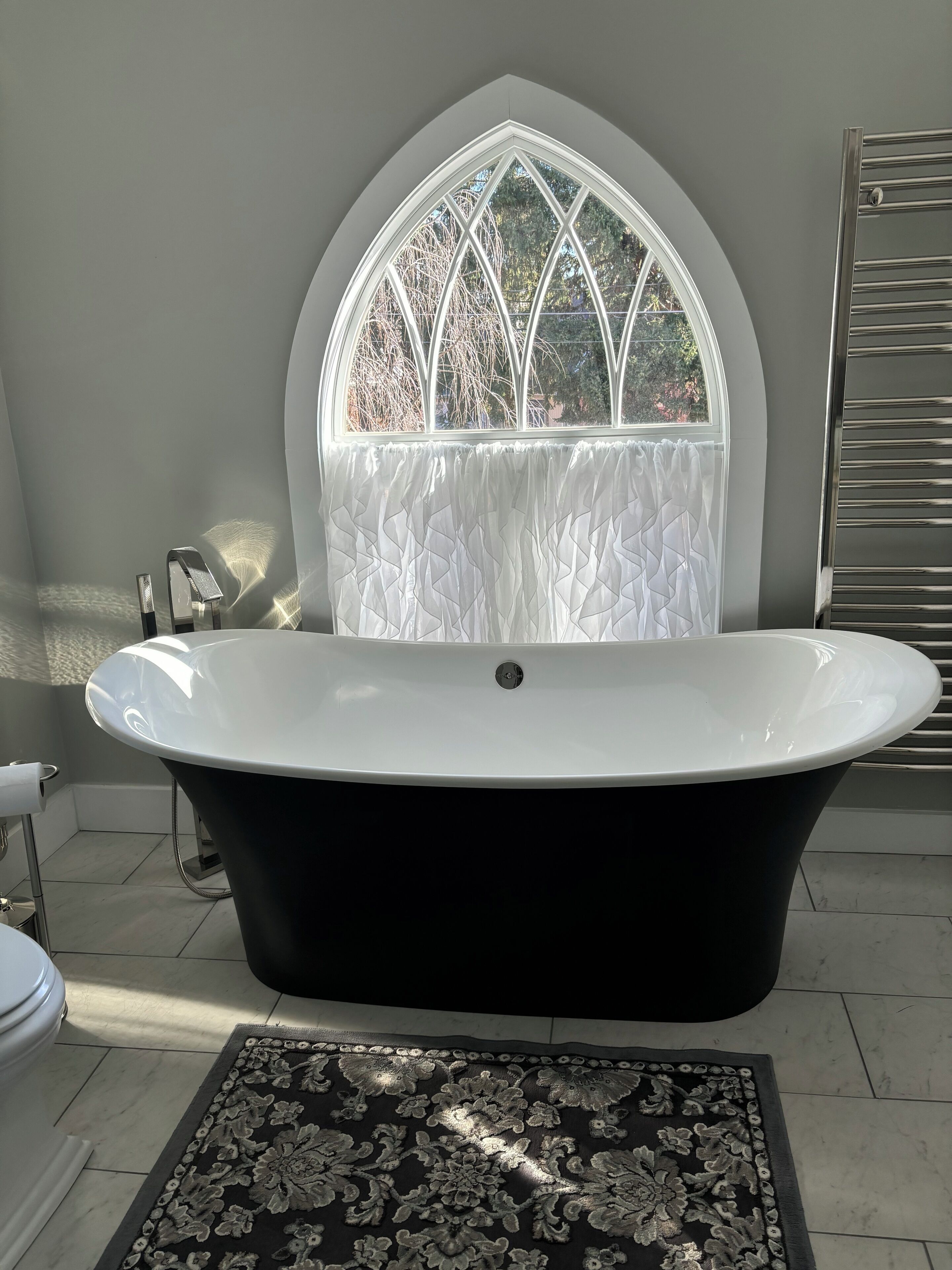 A modern bathroom with a freestanding bathtub, a decorative window, and a patterned rug.