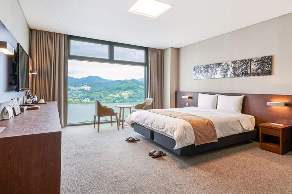 Habitación de hotel con una cama grande, un escritorio, una silla y vistas a las montañas.