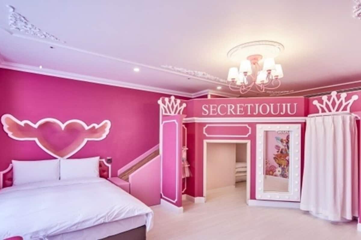 Dormitorio rosa con cama, tocador y escalera.